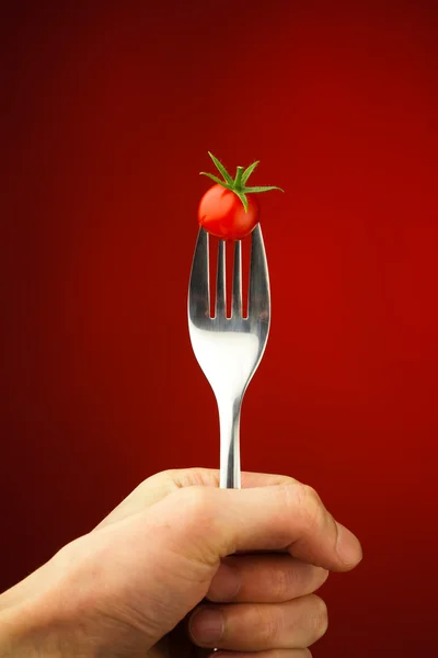 Hand holding a fork with cherry tomato — Stock Photo, Image