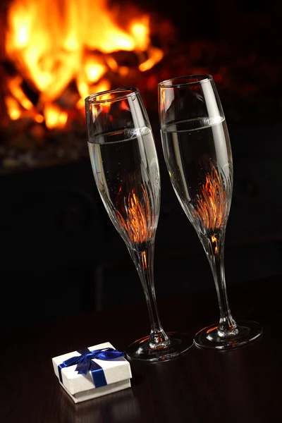 Copos com champanhe e um presente, fogo como fundo — Fotografia de Stock