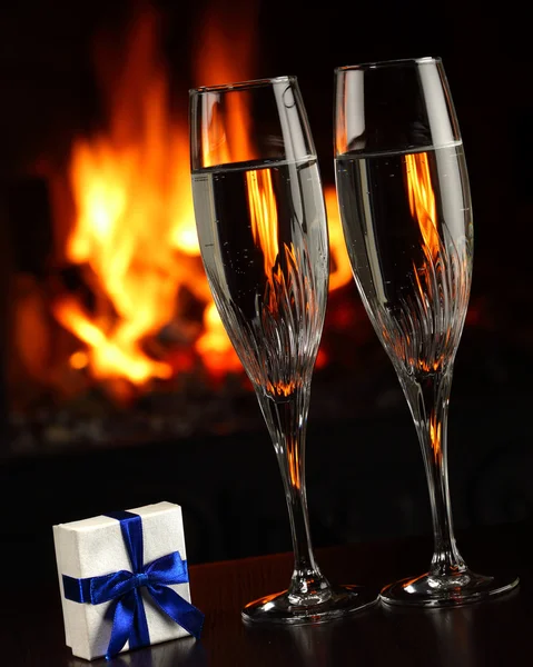 Verres avec champagne et un cadeau, le feu comme fond — Photo