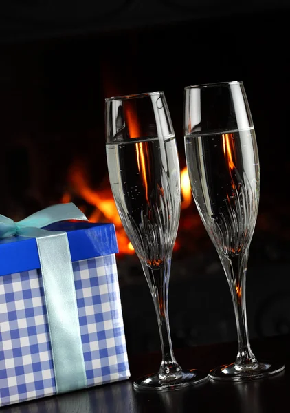 Bardak şampanya ve bir hediye ile ateş arka plan olarak — Stok fotoğraf