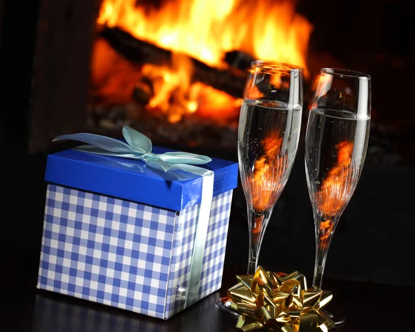 Бокалы с шампанским и подарок, огонь на заднем плане — стоковое фото