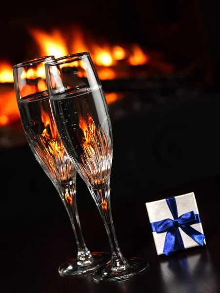 Glasses with champagne and a gift, fire as the background — Stock Photo, Image