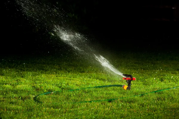 Aspersor de césped rociando agua sobre hierba verde por la noche — Foto de Stock