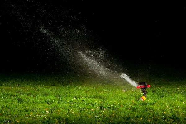 Газонокосарка спринклер розбризкує воду по зеленій траві вночі — стокове фото