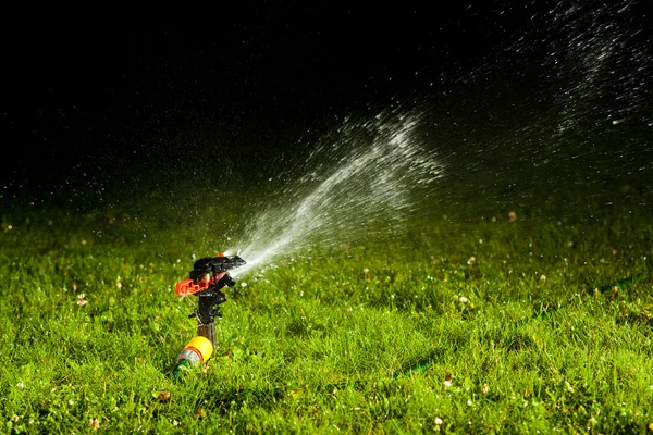 Aspersor de césped rociando agua sobre hierba verde por la noche —  Fotos de Stock
