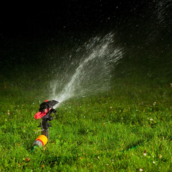 Lawn sprinkler spraying water over green grass at night — Stock Photo, Image