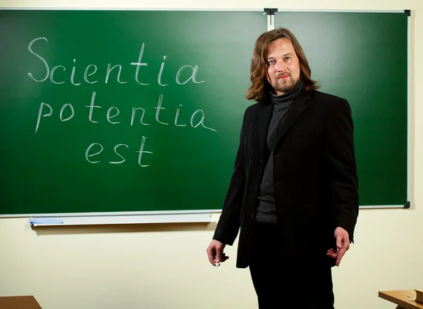 Young teacher against blackboard background — Stock Photo, Image