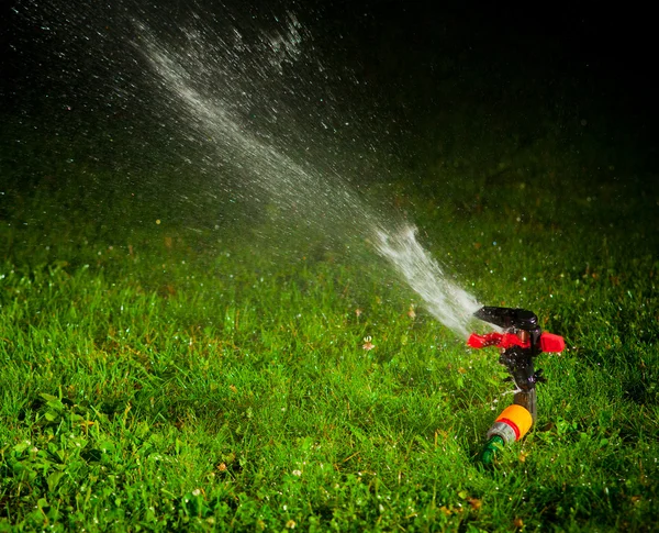 Gräsmatta sprinkler sprutar vatten över grönt gräs på natten — Stockfoto