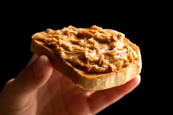 Masło orzechowe Zapiekana bulka chleba w ręku na czarnym tle — Zdjęcie stockowe