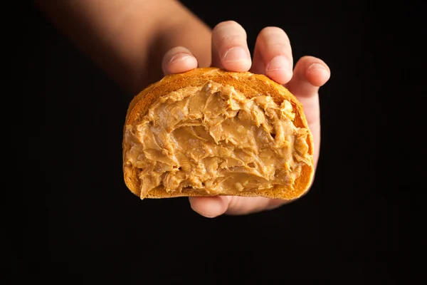 Peanut butter toast bread in hand on black background — Stock Photo, Image