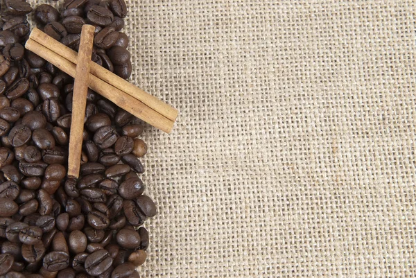Kávová zrna a skořice na pytlovina. — Stock fotografie