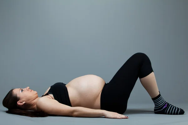 Portret van zwangere brunette vrouw op grijze achtergrond. — Stockfoto