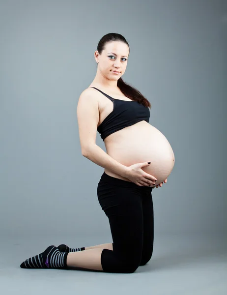 Portret kobiety w ciąży brunetka na szarym tle. — Zdjęcie stockowe