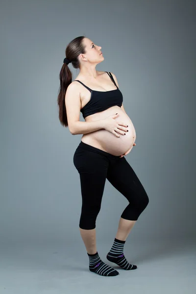 Porträt einer schwangeren brünetten Frau auf grauem Hintergrund. — Stockfoto