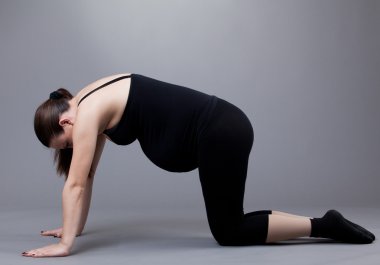 Pregnant woman doing gymnastic exercises on grey background. clipart