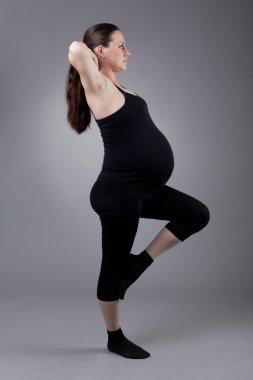 hamile kadın gri arka plan üzerinde jimnastik egzersizleri yapıyor.