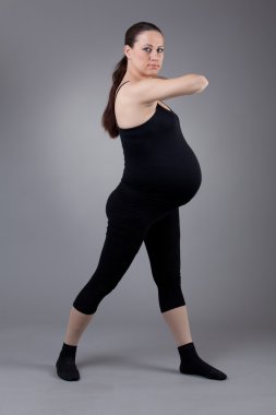 hamile kadın gri arka plan üzerinde jimnastik egzersizleri yapıyor.