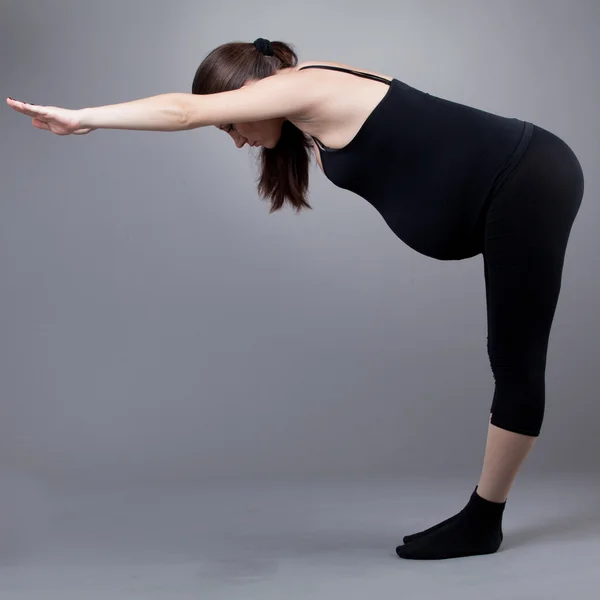 Mujer embarazada haciendo ejercicios de gimnasia sobre fondo gris . —  Fotos de Stock