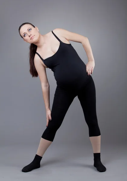 Pregnant woman doing gymnastic exercises on grey background. — Stock Photo, Image
