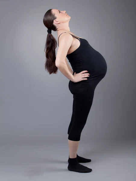 Kobieta w ciąży robi ćwiczenia gimnastyczne na szarym tle. — Zdjęcie stockowe