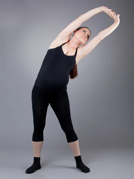 Gravid kvinna gör gymnastiska övningar på grå bakgrund. — Stockfoto