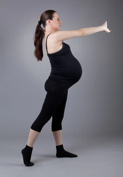 Zwangere vrouw doen gymnastische oefeningen op grijze achtergrond. — Stockfoto