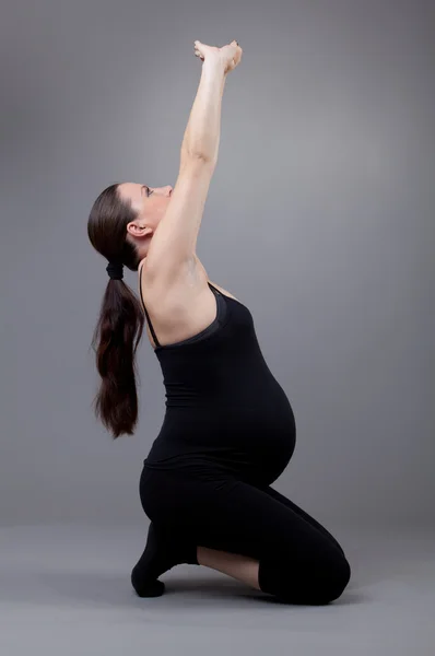 Pregnant woman doing gymnastic exercises on grey background. — Stock Photo, Image