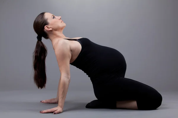 Вагітна жінка робить гімнастичні вправи на сірому фоні . — стокове фото