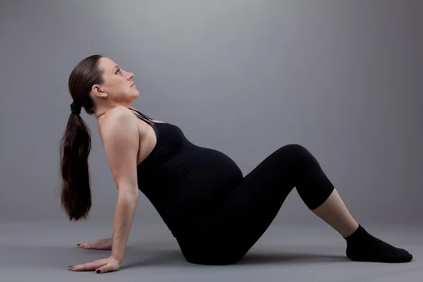 Mulher grávida fazendo exercícios de ginástica em fundo cinza . — Fotografia de Stock