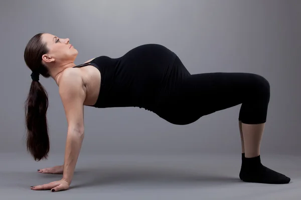 Femme enceinte faisant des exercices de gymnastique sur fond gris . — Photo