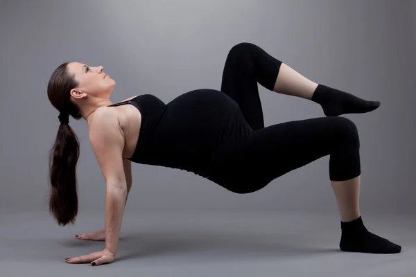 Gravid kvinna gör gymnastiska övningar på grå bakgrund. — Stockfoto