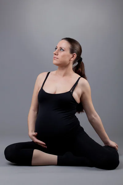 Беременная женщина делает гимнастические упражнения на сером фоне . — стоковое фото
