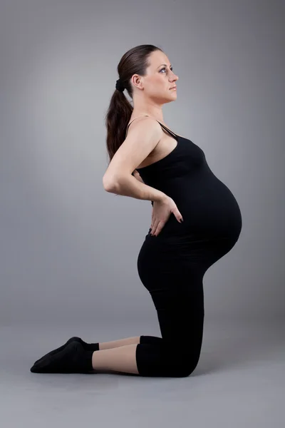 Pregnant woman doing gymnastic exercises on grey background. — Stock Photo, Image