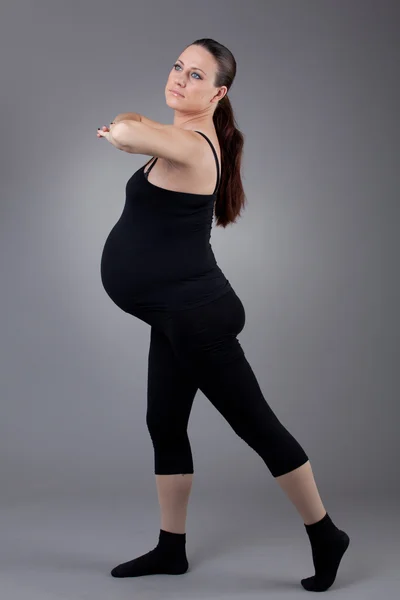 Těhotná žena, která dělá gymnastické cvičení na šedém pozadí. — Stock fotografie