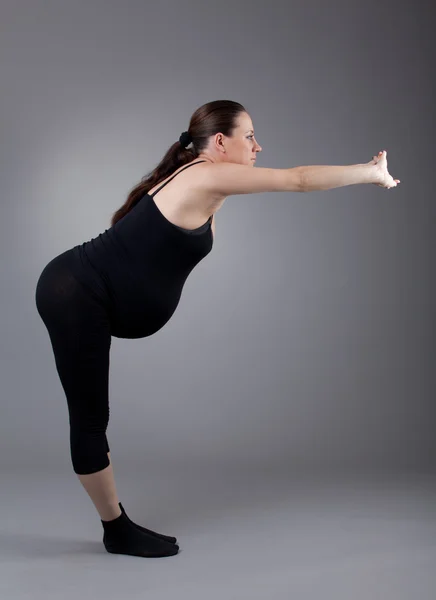 Terhes nő csinál gimnasztikai gyakorlatokat a szürke háttér. — Stock Fotó