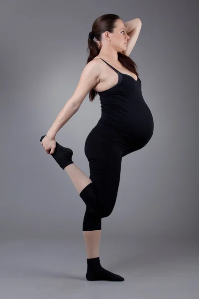 Έγκυος γυναίκα κάνει γυμναστικές ασκήσεις, σε γκρι φόντο. — Φωτογραφία Αρχείου