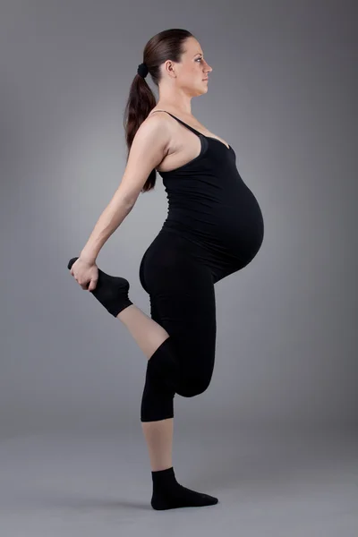 Femme enceinte faisant des exercices de gymnastique sur fond gris . — Photo