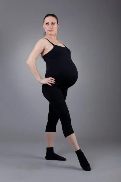 Беременная женщина делает гимнастические упражнения на сером фоне . — стоковое фото