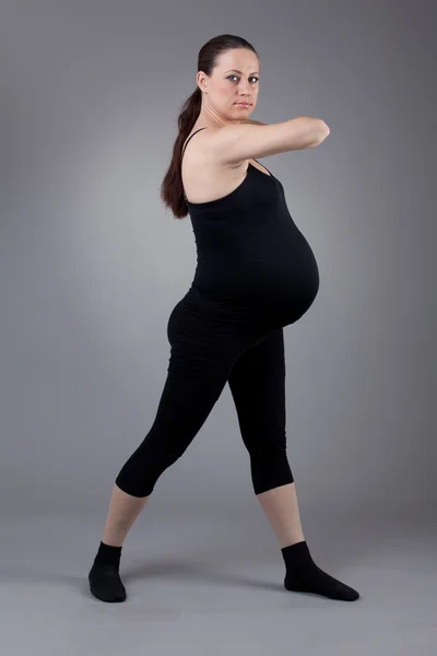 Mujer embarazada haciendo ejercicios de gimnasia sobre fondo gris . — Foto de Stock