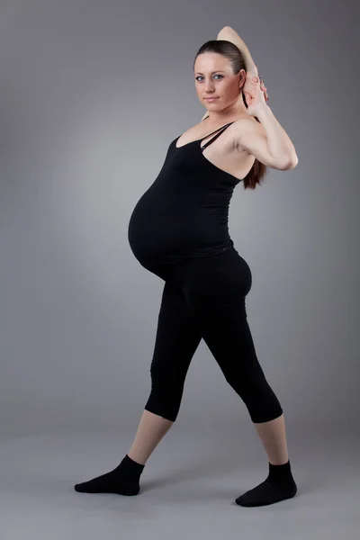 Donna incinta che fa esercizi ginnici su sfondo grigio . — Foto Stock