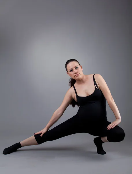 stock image Pregnant woman doing gymnastic exercises on grey background.