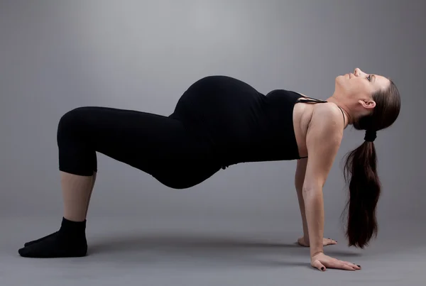 Kobieta w ciąży robi ćwiczenia gimnastyczne na szarym tle. — Zdjęcie stockowe