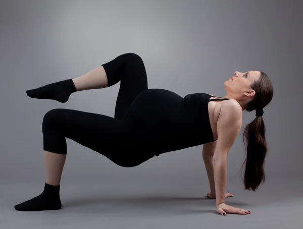 Terhes nő csinál gimnasztikai gyakorlatokat a szürke háttér. — Stock Fotó
