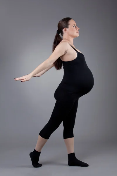 Zwangere vrouw doen gymnastische oefeningen op grijze achtergrond. Rechtenvrije Stockafbeeldingen