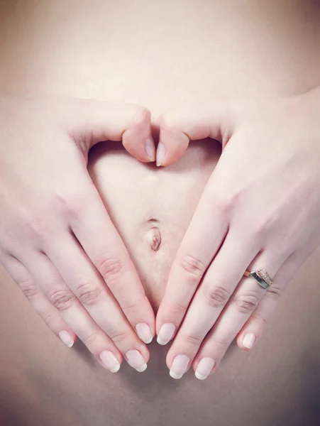 Closeup δάχτυλα σε σχήμα καρδιάς πάνω από τον ομφαλό σε λευκό εγκύου κοιλιά. συλλογή της εγκυμοσύνης. — Φωτογραφία Αρχείου