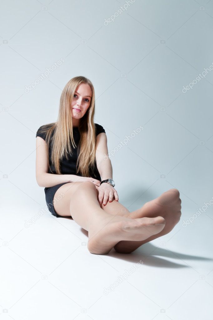 Pretty lady sitting on the floor. Wearing fashionable dress and tights. Fresh new young face. Studio shot, uniform background