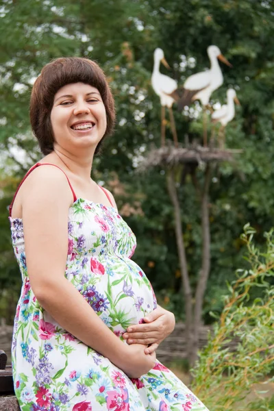 Молодая и счастливая беременная женщина со скульптурой из аистов — стоковое фото
