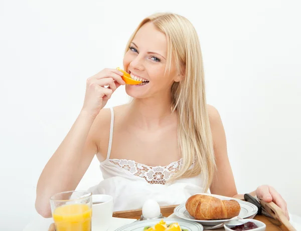 Beautiful woman eating orange in bed — Stock Photo, Image