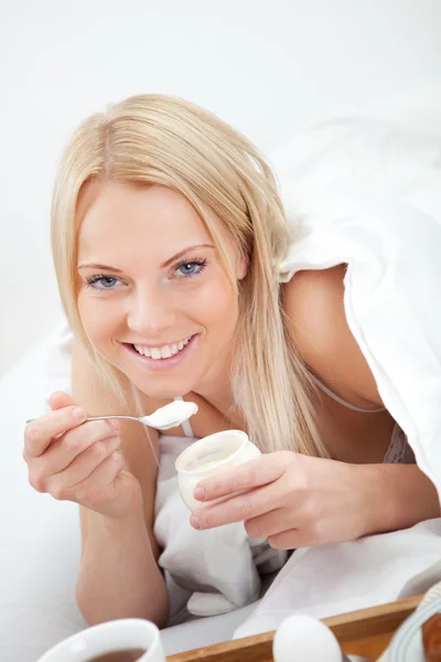 Beautiful woman eating yogurt in bed — Stock Photo, Image