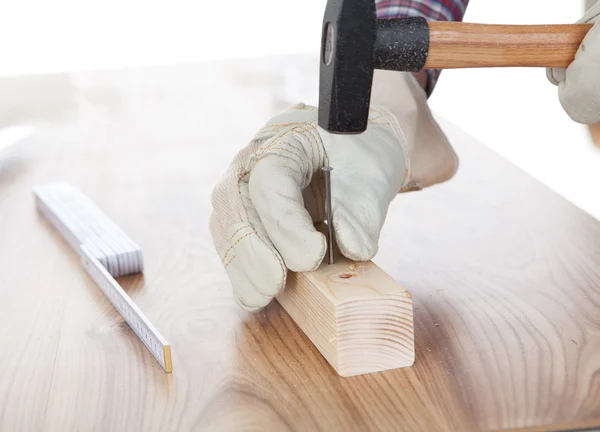 Travailleur martelant un clou dans un morceau de bois — Photo